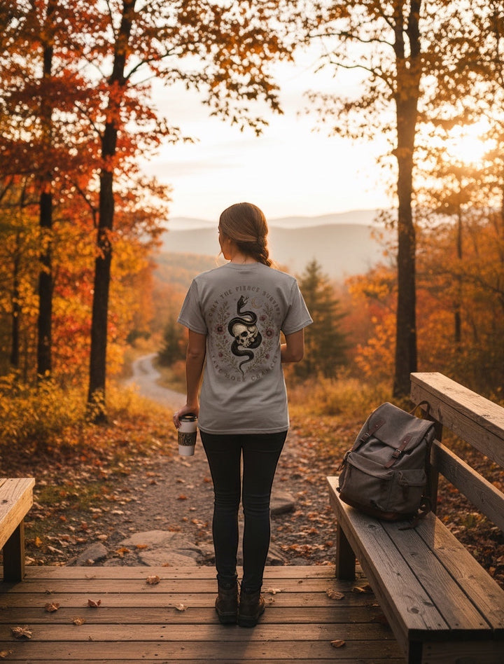 JSD Apparel unisex tee with skull and serpent back graphic, worn by a woman on a scenic autumn forest trail.