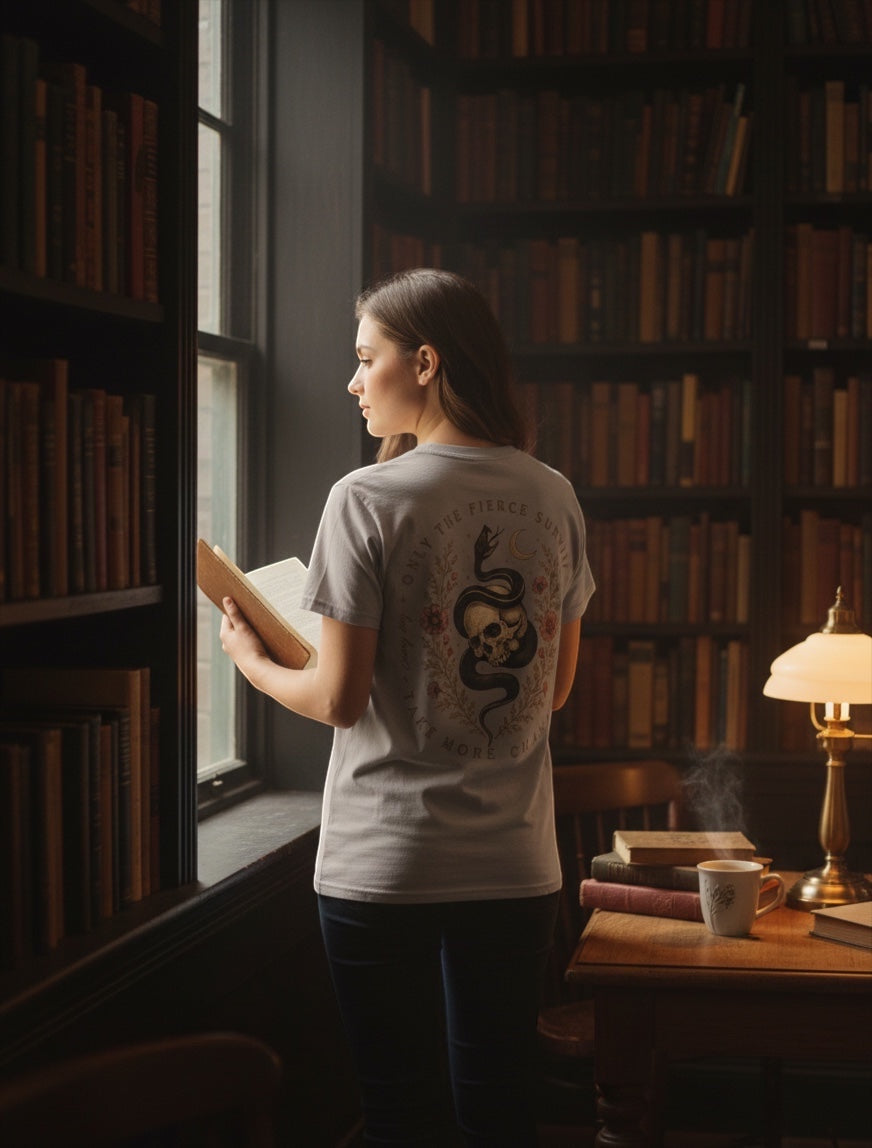 JSD Apparel unisex tee with skull and serpent back graphic, worn by a woman reading in a vintage library setting.