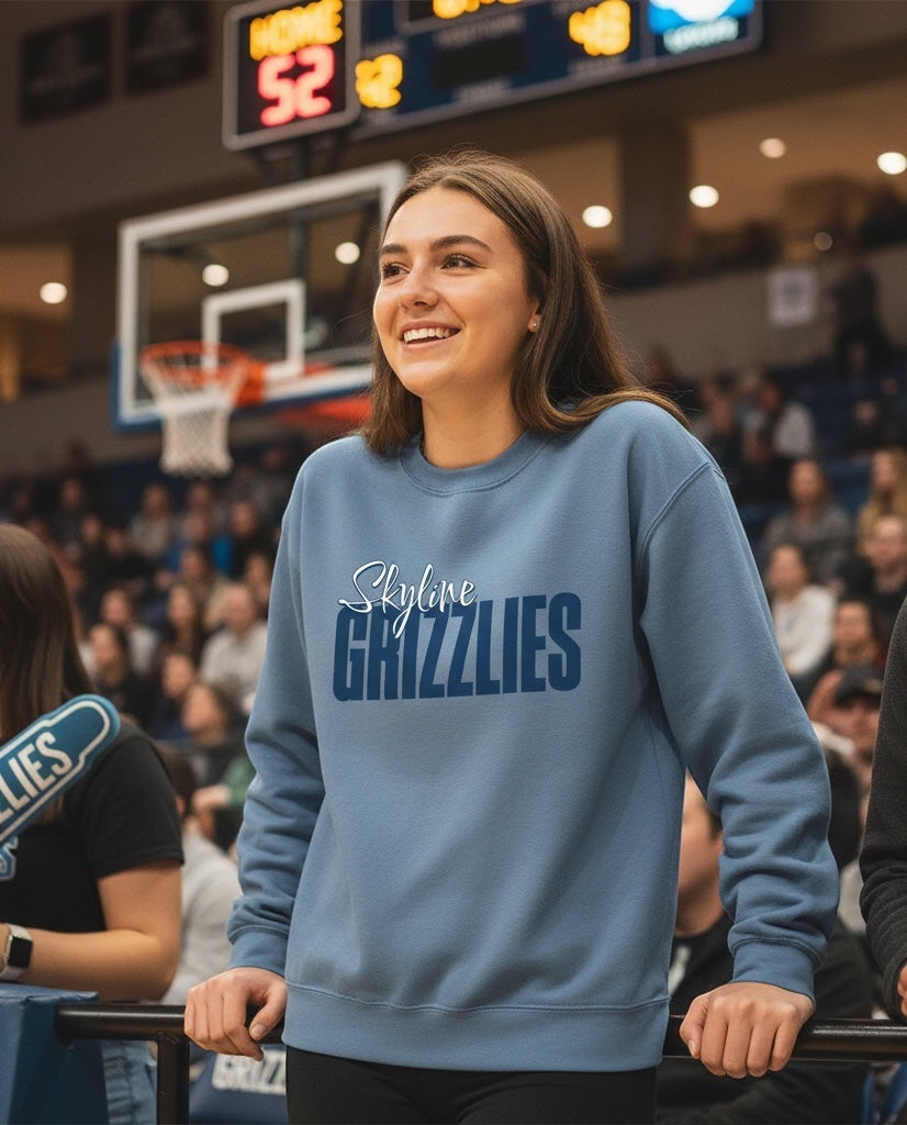 Woman wearing a blue JSD Apparel Skyline Grizzlies crewneck sweatshirt with script and block lettering at a game.