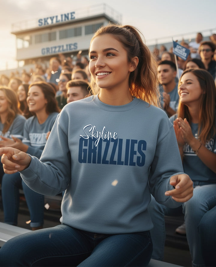 A woman wearing a JSD Apparel blue crewneck sweatshirt with Skyline Grizzlies script logo at a crowded sports stadium.