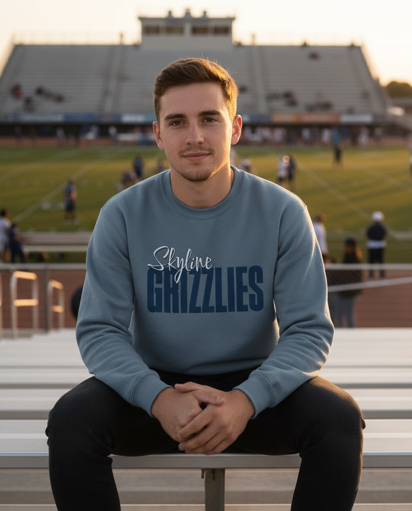 A man wearing a blue JSD Apparel crewneck sweatshirt with Skyline Grizzlies script logo, sitting in a stadium.