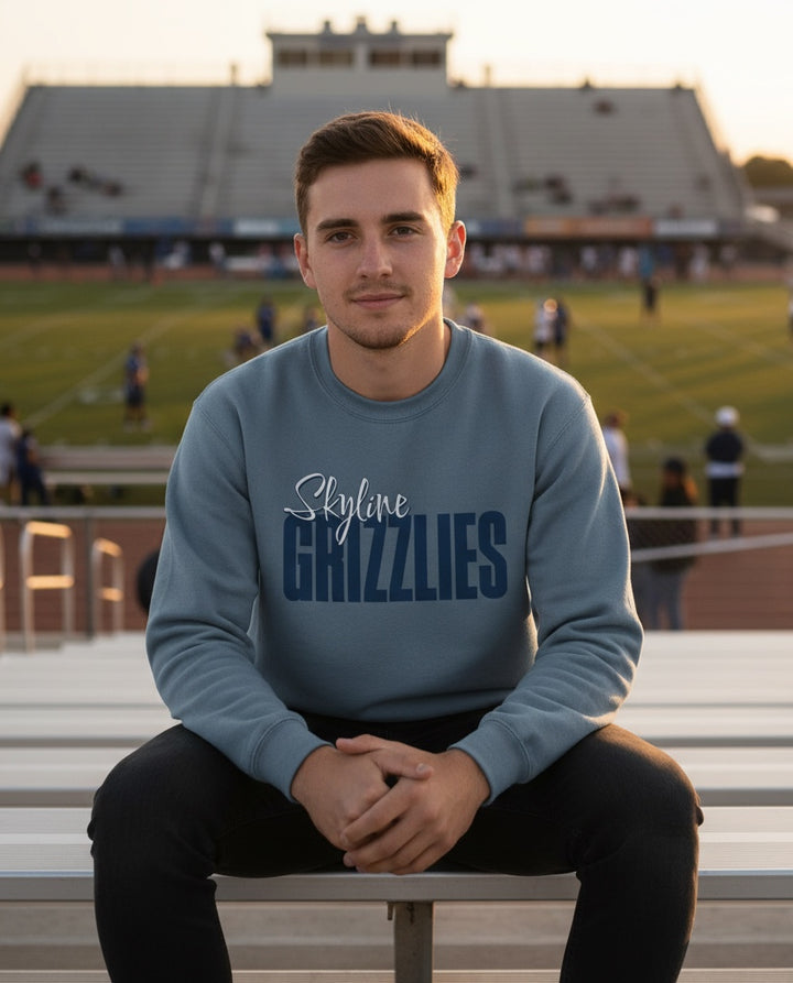 A man wearing a blue JSD Apparel crewneck sweatshirt with Skyline Grizzlies script logo, sitting in a stadium.