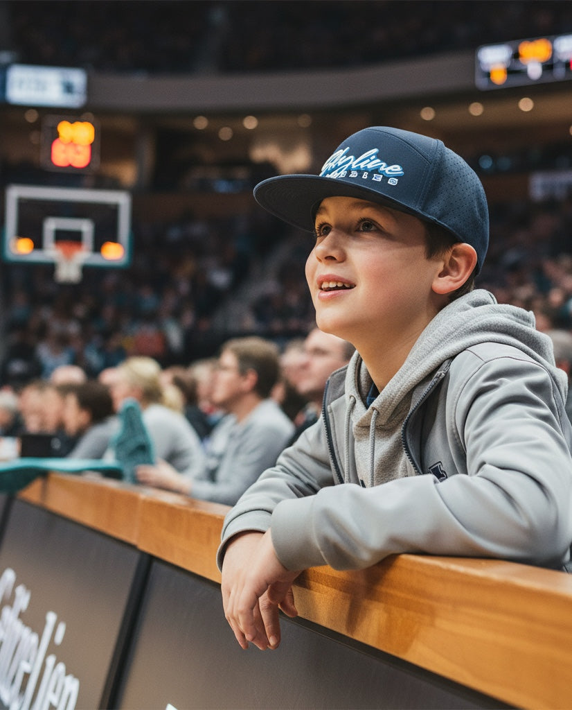 A young boy wearing a navy JSD Apparel Skyline Grizzlies performance snapback cap at a basketball game.