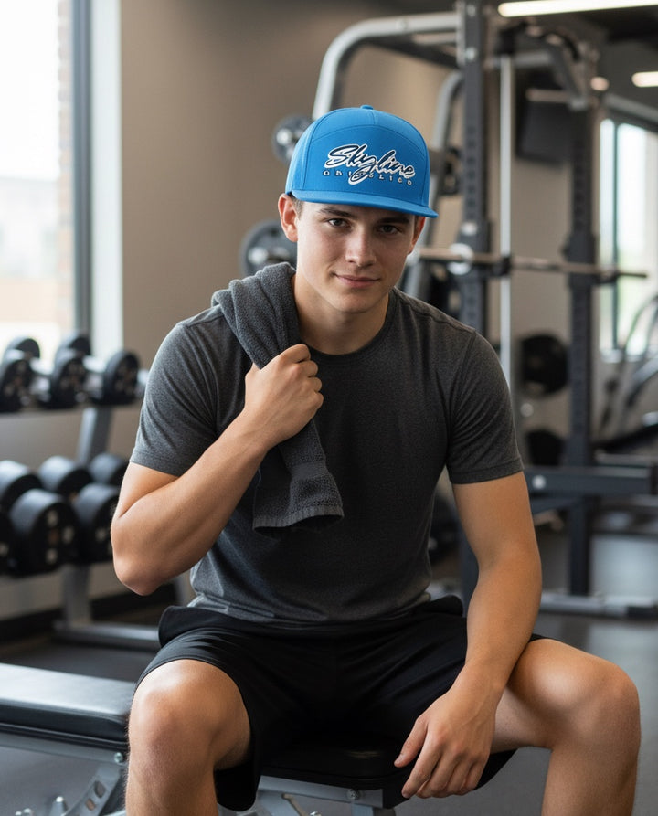Man wearing a blue JSD Apparel Skyline Grizzlies performance cap with a flat bill in a gym setting.