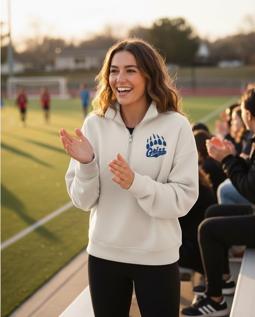 A woman wearing a JSD Apparel Skyline Grizzlies cream quarter-zip fleece pullover with a blue paw logo at a sports game