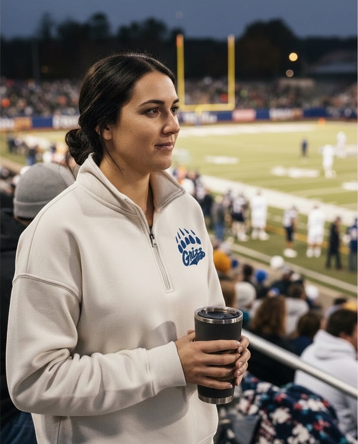 Woman wearing a JSD Apparel Skyline Grizzlies quarter zip fleece pullover with a blue paw logo at a football game.