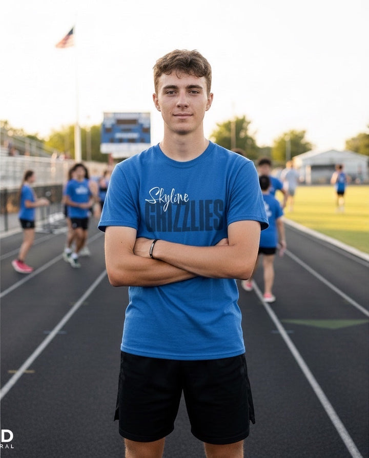 Male student wearing a blue JSD Apparel Skyline Grizzlies script tee on a track field with other students.