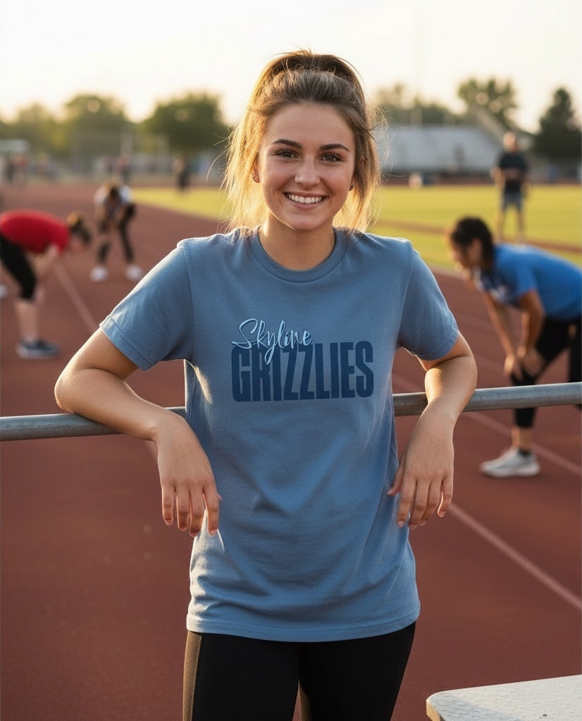 Woman wearing a blue JSD Apparel Skyline Grizzlies cotton tee with script lettering on a track field.