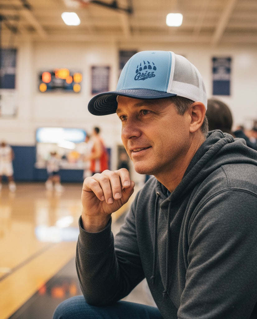 Man wearing a JSD Apparel Skyline Grizzlies blue and white mesh trucker hat with a paw logo in a basketball gym.