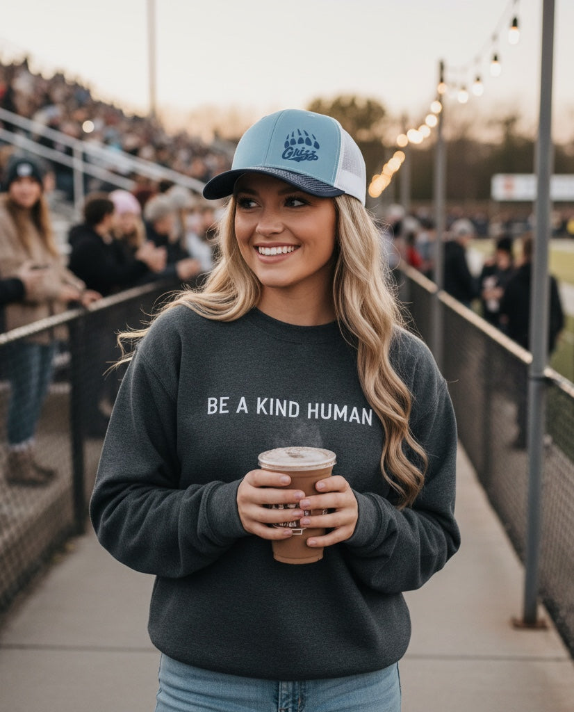 JSD Apparel Skyline Grizzlies paw trucker hat in blue and white worn by a smiling woman at a stadium.