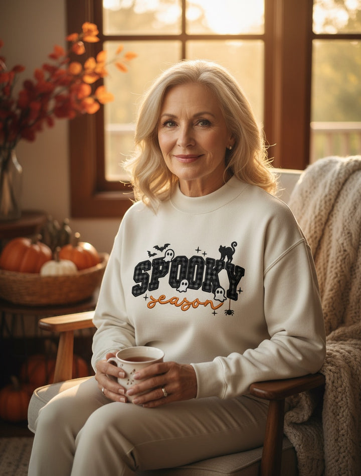 JSD Apparel Spooky Season mock neck sweatshirt with plaid lettering and Halloween icons on a woman in a cozy room.