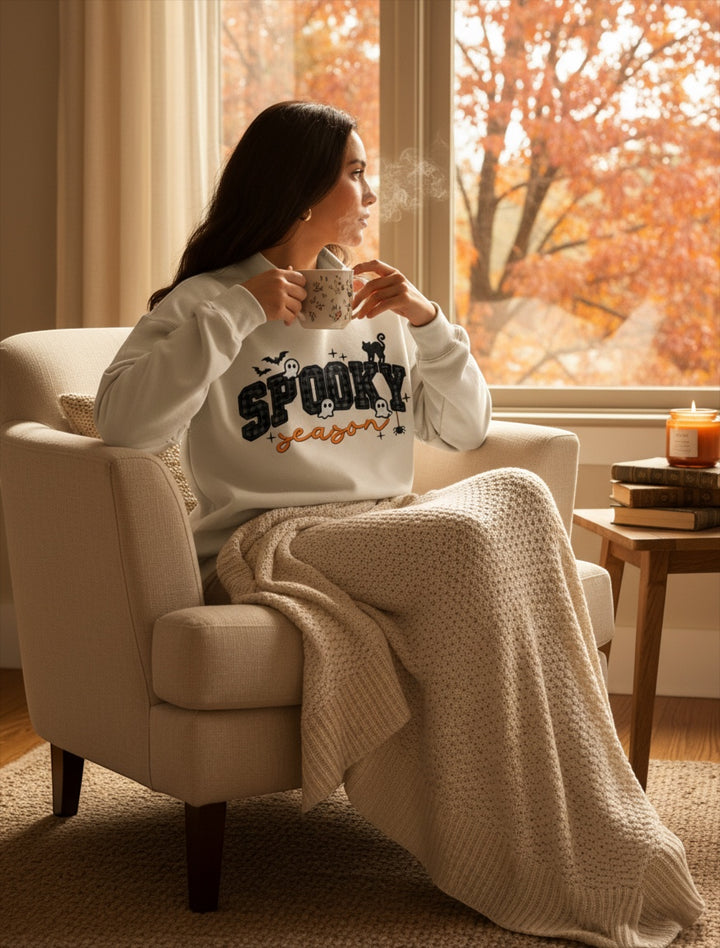 JSD Apparel Spooky Season mock neck sweatshirt with plaid lettering and Halloween graphics on a woman in a cozy chair