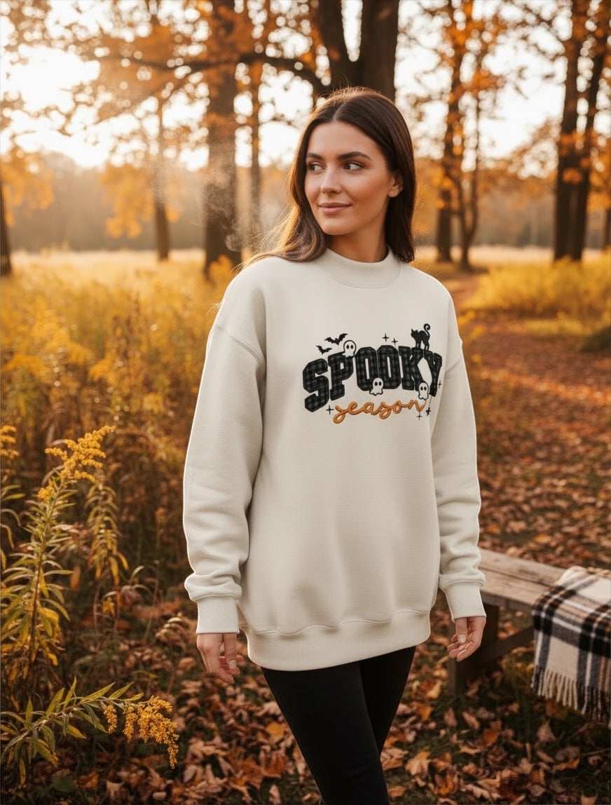 JSD Apparel cream mock neck sweatshirt with Spooky Season varsity plaid print, worn by a woman in an autumn forest.