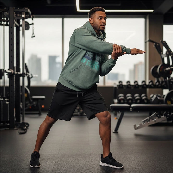 JSD Apparel Drift & Endure storm blue cotton-blend hoodie with graphic print worn by a man stretching in a gym.