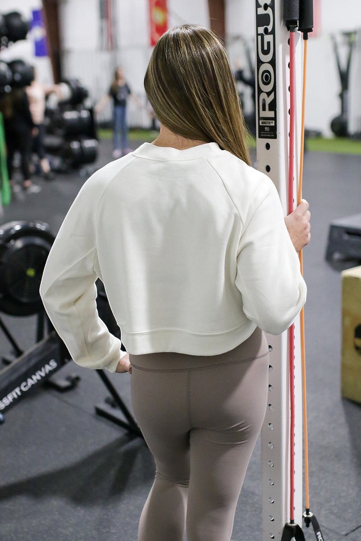 JSD Apparel white cropped fleece pullover with raglan sleeves worn by a woman in a gym setting