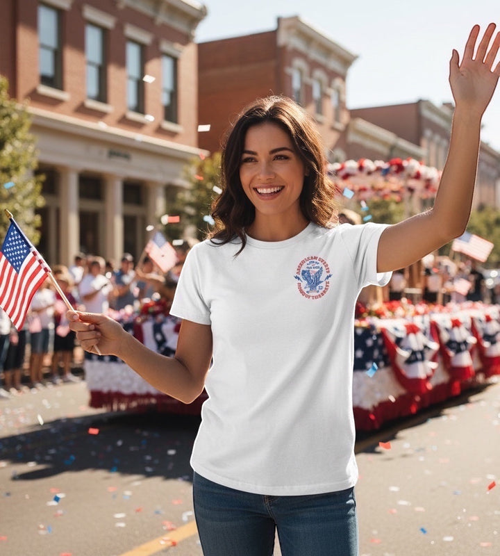 JSD Apparel white cotton t-shirt with vintage eagle graphic worn by a woman waving an American flag at a parade.